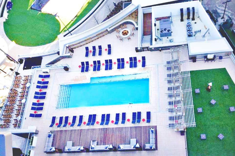 Aerial view of resort pool surrounded by blue and white lounge chairs, green lawn areas, and white buildings