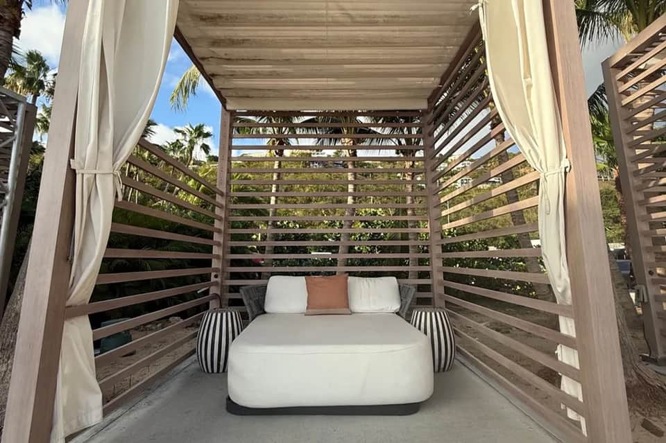 Wooden bed canopy with slatted sides and flowing white curtains on outdoor patio