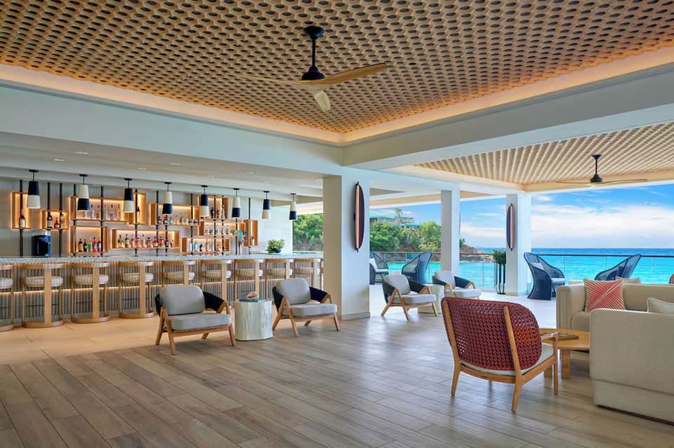 Upscale beachfront bar lounge with wooden accents, ocean views, wicker seating, and panoramic windows