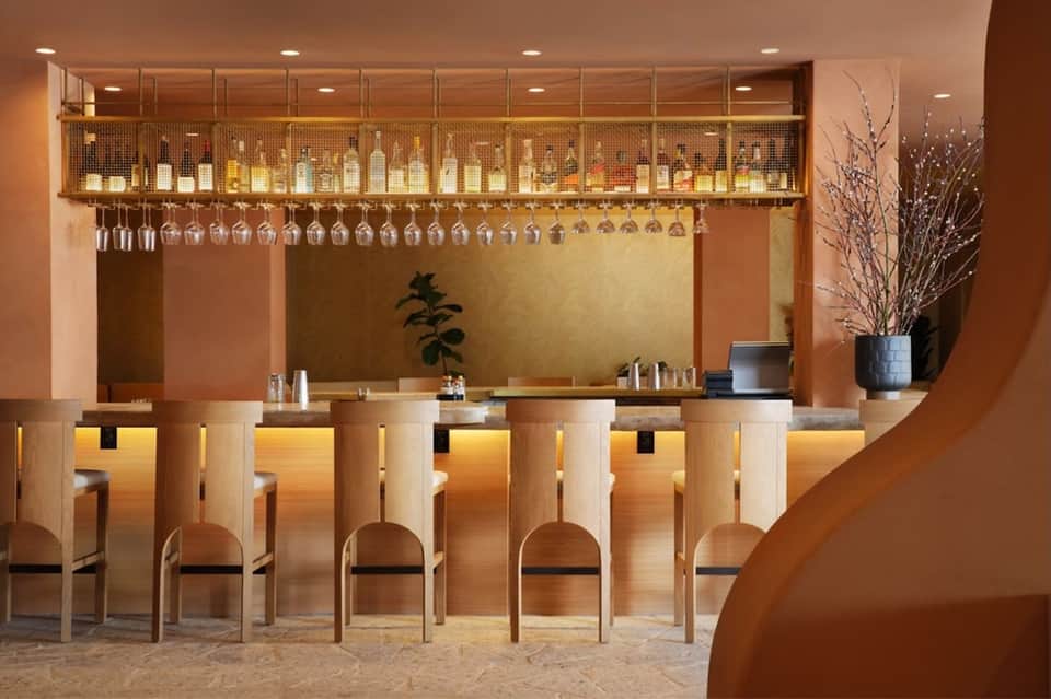 Elegant bar counter with wood paneling, hanging glassware, and bottles displayed on illuminated upper shelf