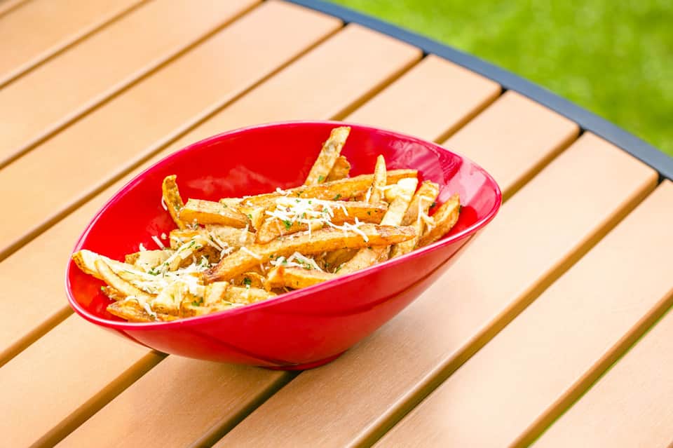 Red bowl of seasoned french fries on wooden deck by pool area