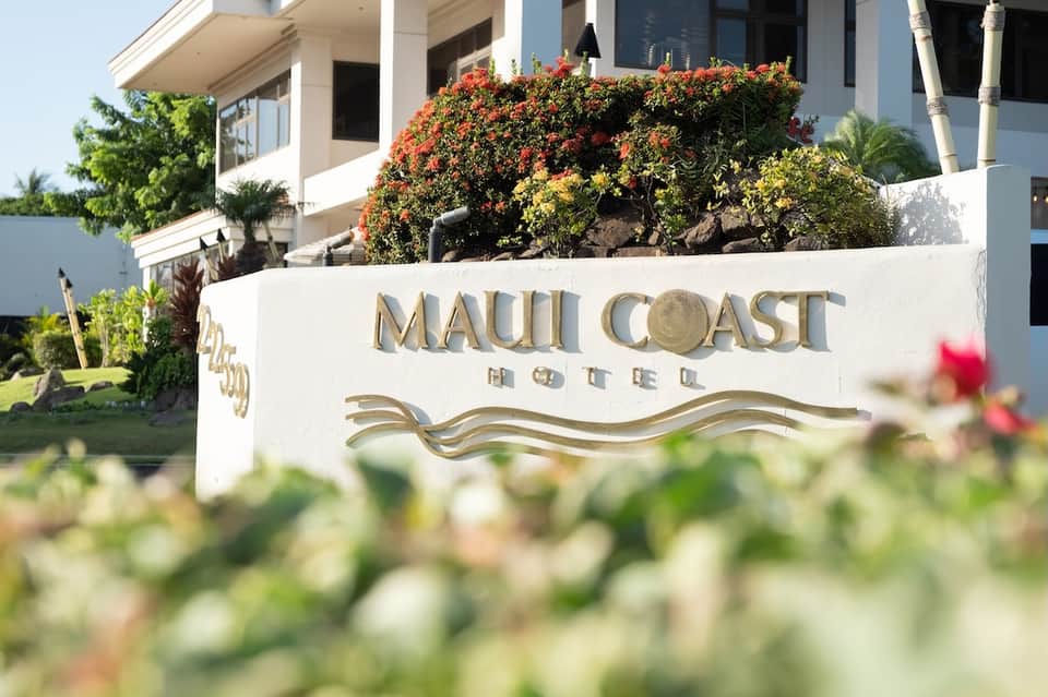 Maui Coast Hotel exterior sign with colorful flowering plants and modern building architecture