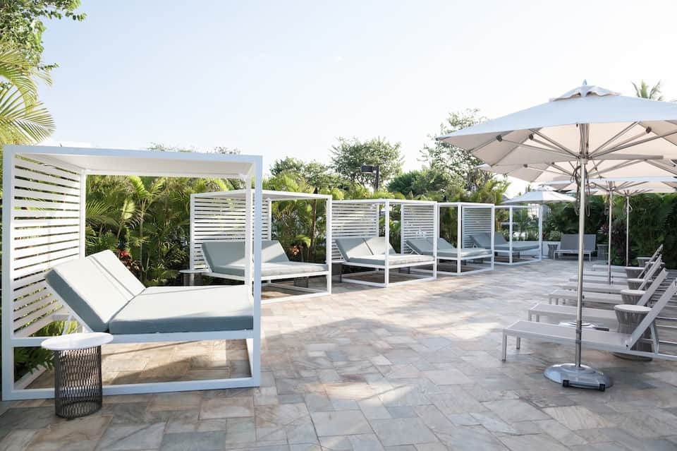 Luxury resort patio with lounge beds, pergola, umbrellas, and lush landscaping