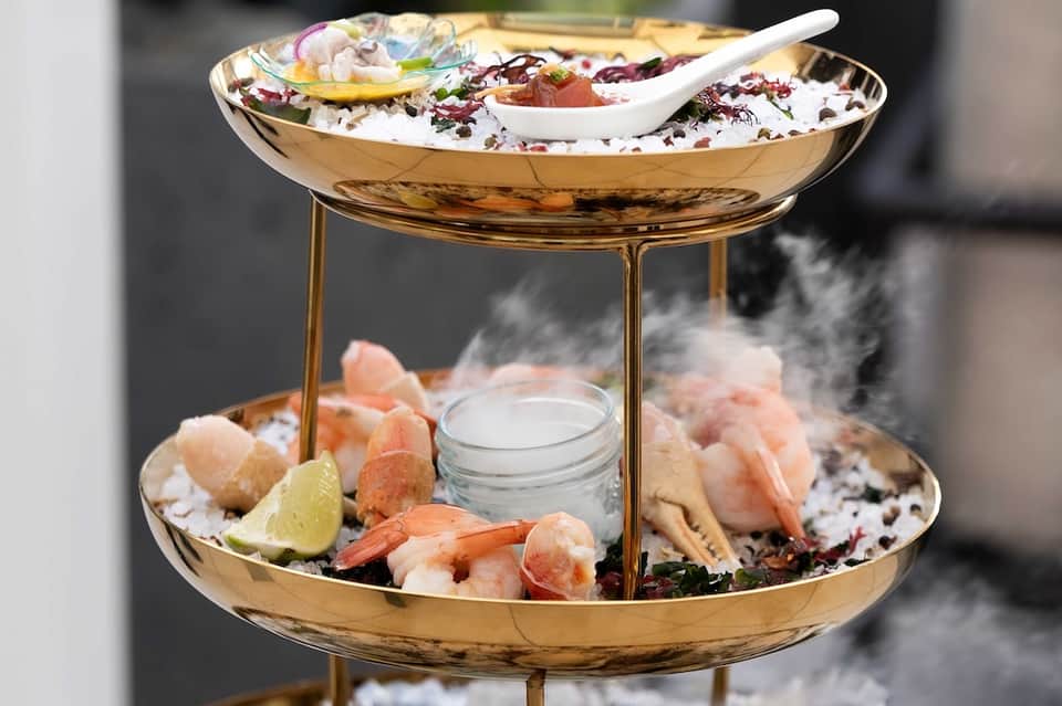 Luxury seafood tower with two gold tiers displaying fresh oysters, shrimp, and garnishes