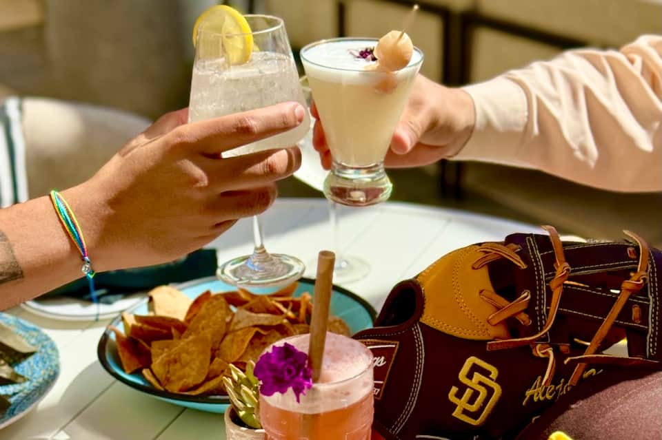 Guests clinking cocktail glasses at dining table with San Diego Padres baseball glove and appetizers