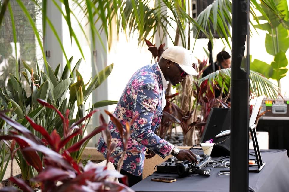 DJ performing in tropical outdoor venue with palm plants and lush island scenery