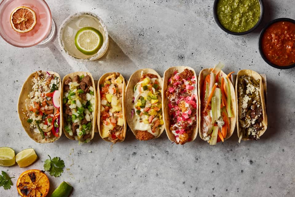 Colorful tacos with various toppings arranged on concrete surface with citrus garnish