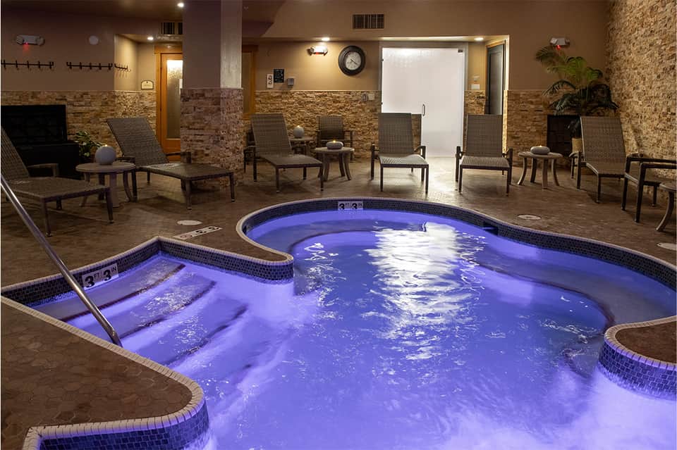 Indoor spa with illuminated hot tub, lounge chairs, and stone accents