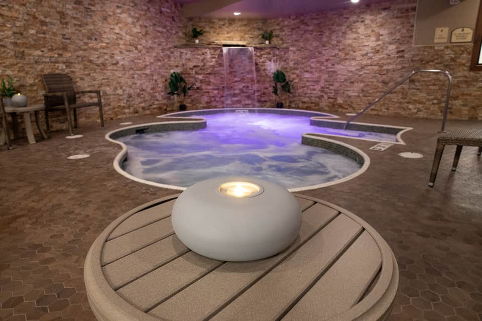 Indoor spa area with illuminated purple hot tub, waterfall feature, and brick walls