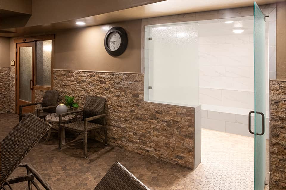 Spa steam room entrance with stone walls and glass shower enclosure beside seating area