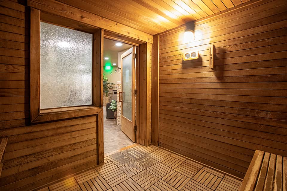 Wooden sauna interior with glass door, bench seating, and textured wood paneling throughout