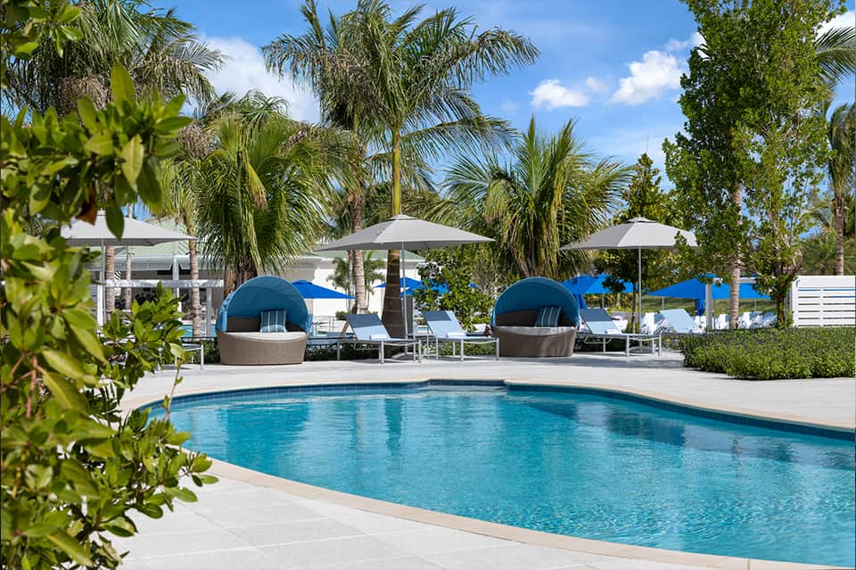 Luxury resort pool with blue water, modern lounge chairs, dome-shaped seating pods, umbrellas, manicured landscaping