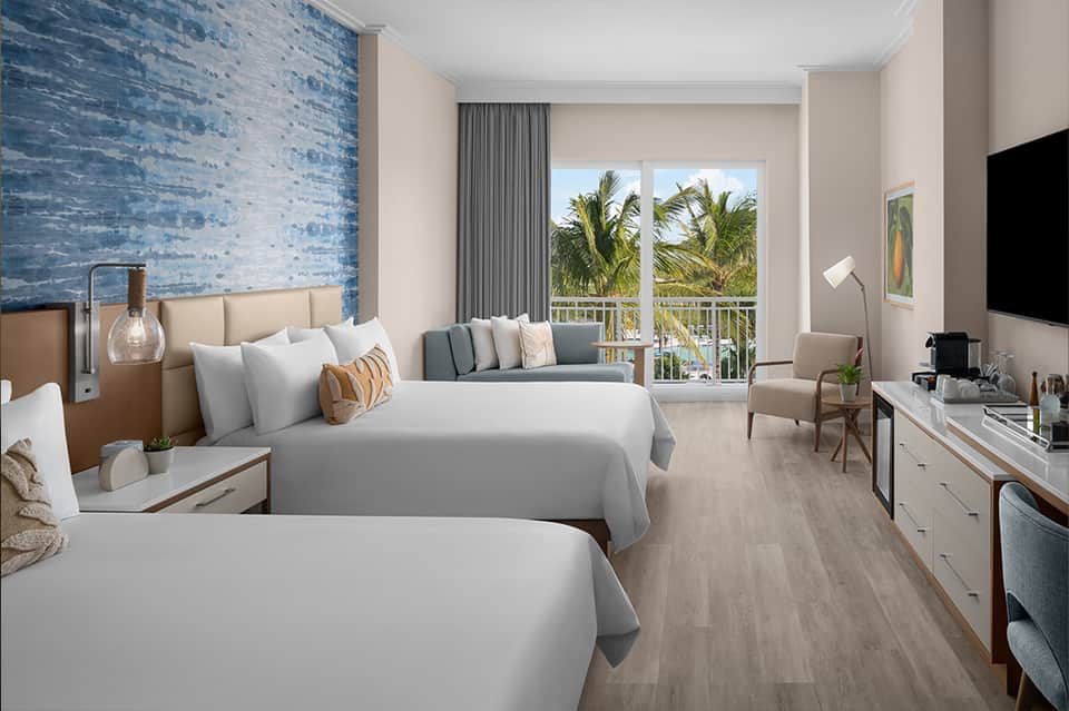 Bright oceanview hotel room with two queen beds, blue accent wall, balcony, and contemporary decor
