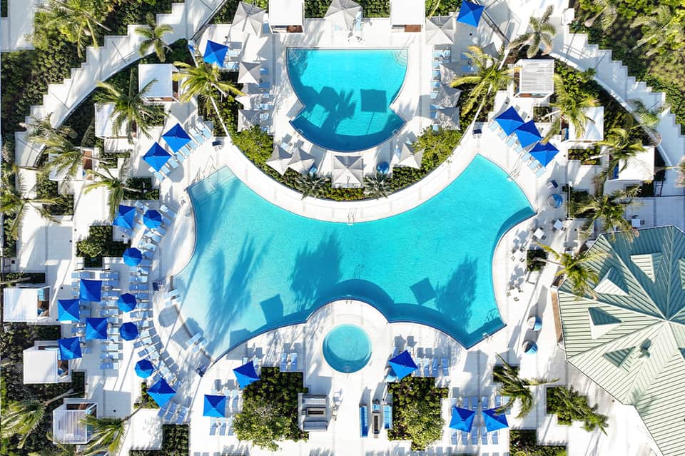 Aerial view of resort pools and white umbrellas surrounded by palm trees