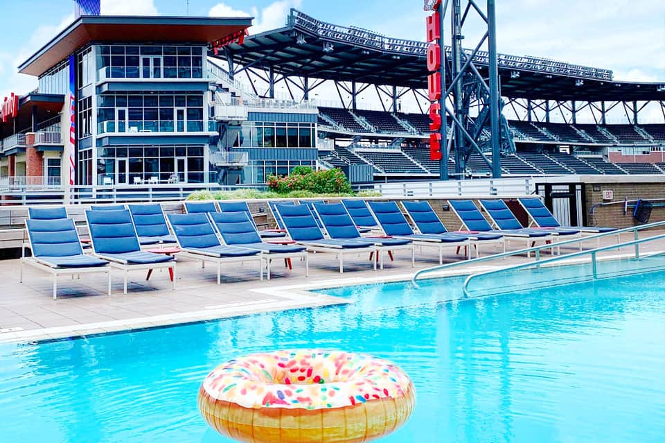Modern sports facility with blue lounge chairs, swimming pool, donut float, and stadium seating