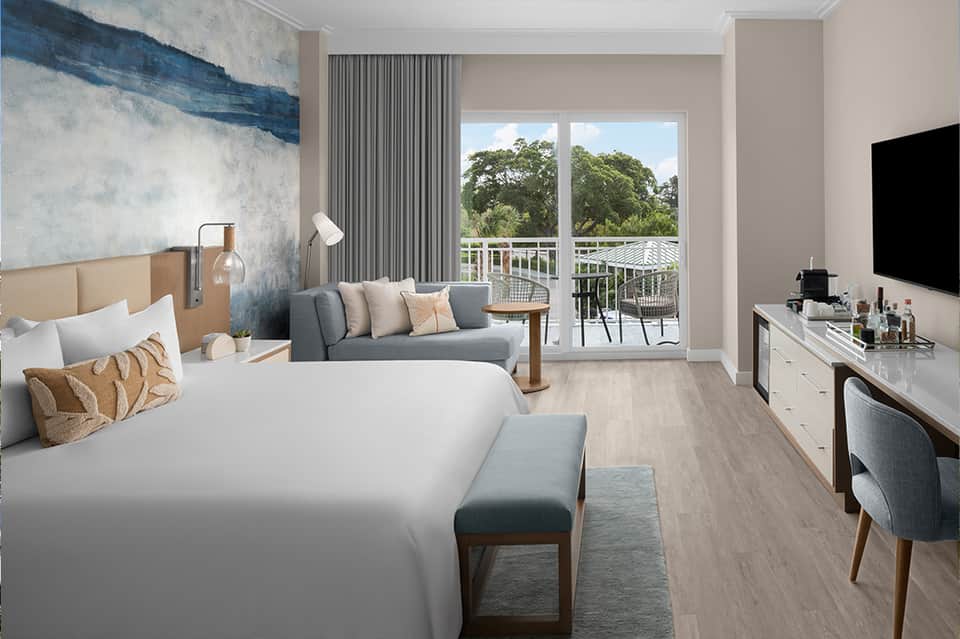 Modern hotel bedroom with balcony view of trees and seating area with artwork