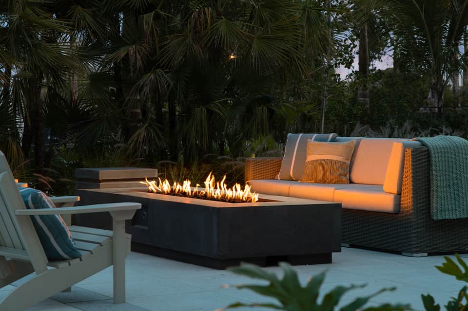 Outdoor lounge area with fire pit, orange cushioned seating, and tropical palm trees