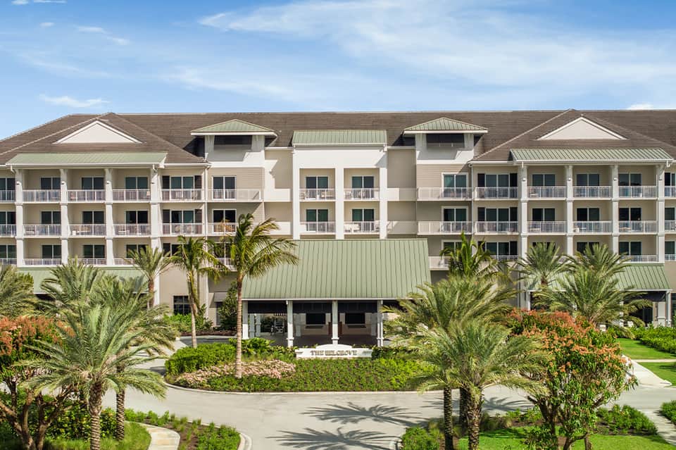Multi-story beachfront resort with white balconies, palm trees, and manicured landscaping