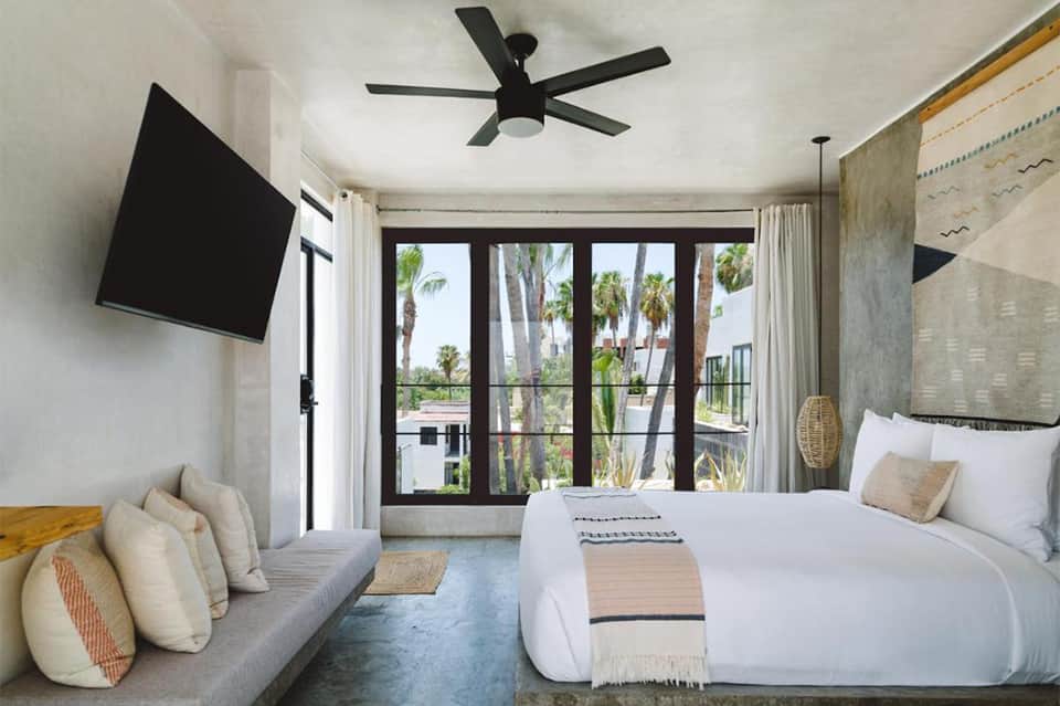 Modern resort bedroom with bed, seating area, flat-screen TV, and sliding glass doors opening to palm tree views