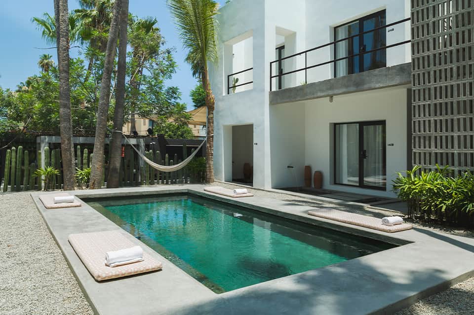Contemporary poolside villa with turquoise water, palm trees, modern white architecture, and hammock