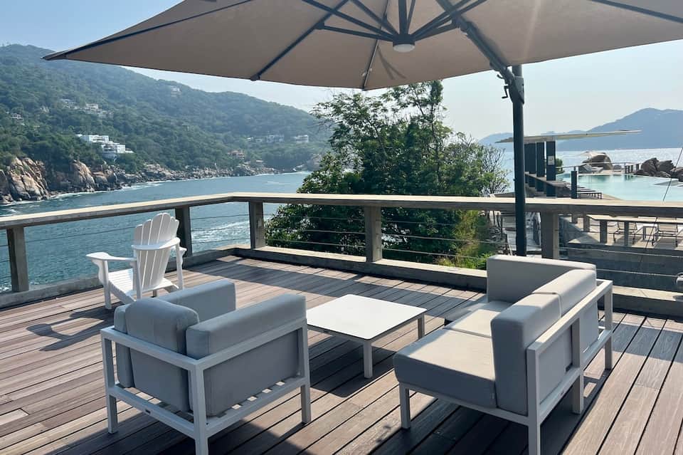 Waterfront deck with modern furniture and umbrella overlooking scenic bay with forested cliffs
