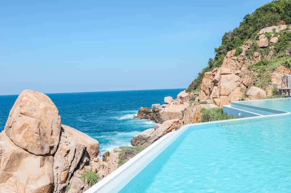 Infinity pool overlooking rocky coastline and turquoise ocean with vegetation-covered cliff
