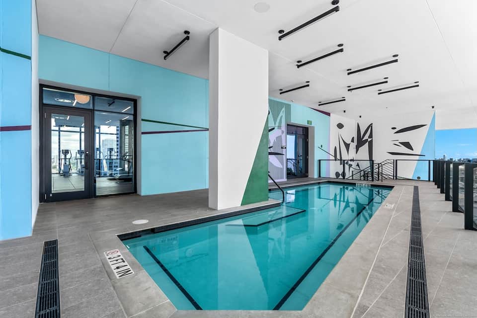 Modern indoor lap pool with turquoise water, geometric wall art, and glass doors