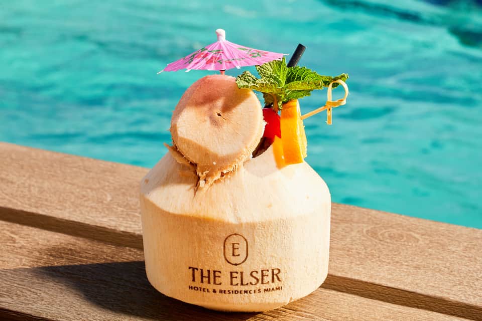 Tropical coconut drink with pink umbrella and garnish branded with The Elster Miami hotel logo