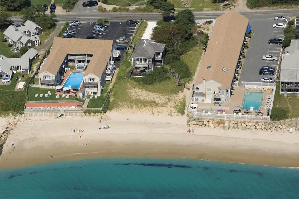 Aerial view of beachfront resort with pools, cottages, parking, and sandy beach