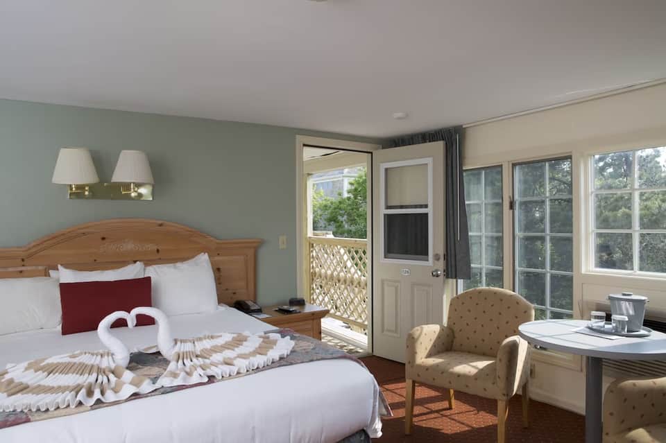 Hotel bedroom with wooden bed frame, mint green accent wall, balcony access, and sitting area with armchair