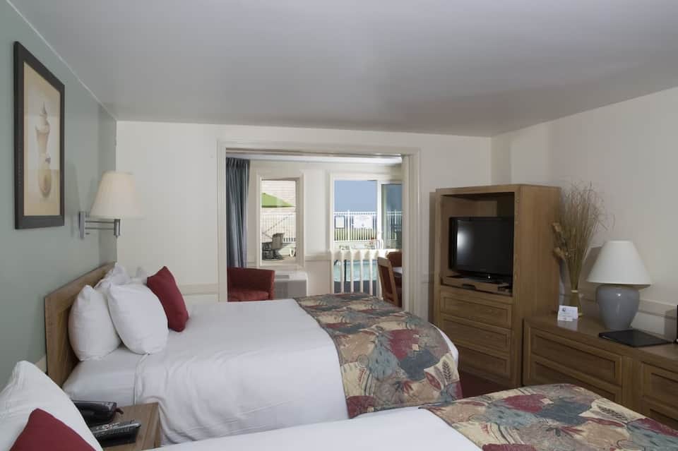 Spacious hotel room with queen beds, ocean view balcony, TV, and warm neutral decor