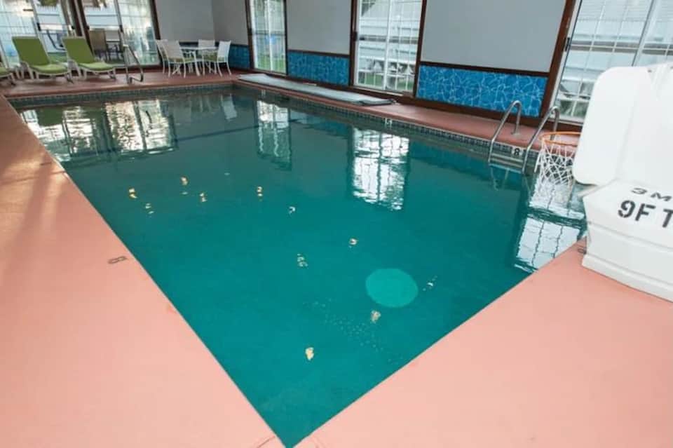 Indoor lap pool with teal water, pink deck, large windows, and lounge chairs in bright indoor facility