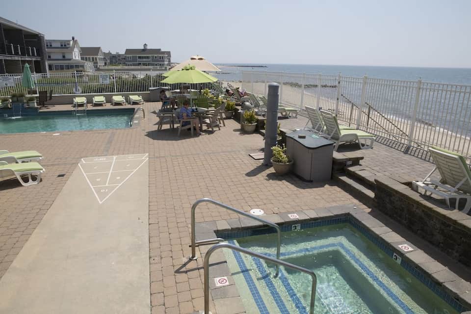 Oceanfront pool deck with Adirondack chairs, umbrella, fire pit, and beach view