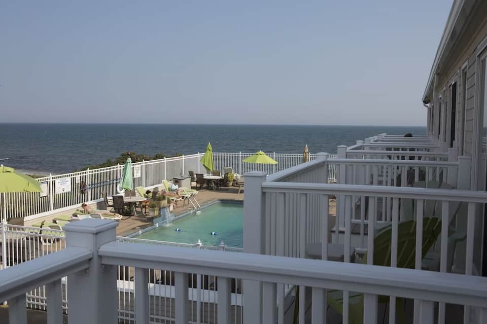 Ocean-view deck with small pool, lounge chairs, white railings, and calm sea horizon in background