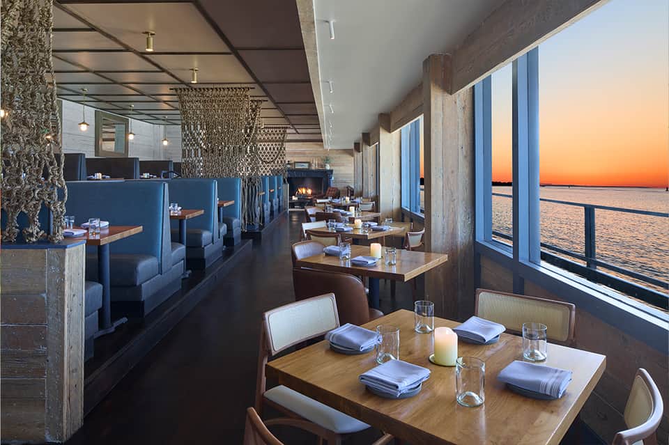 Contemporary restaurant with blue banquettes, wooden tables, and sunset ocean views