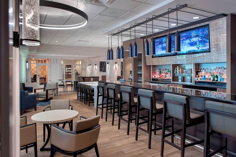 Contemporary hotel bar and lounge with blue pendant lights, full bar, and seating area