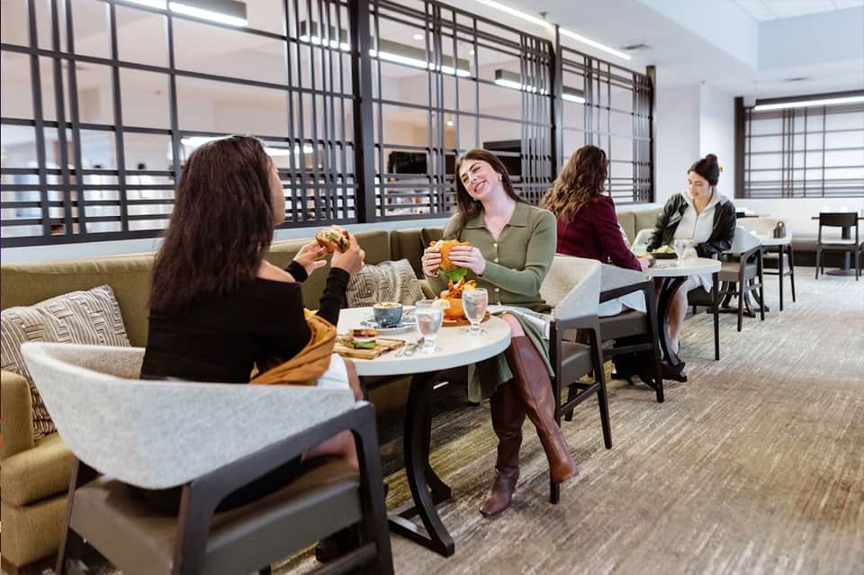 Modern lounge area with guests dining, contemporary furniture, glass partitions, and bright windows