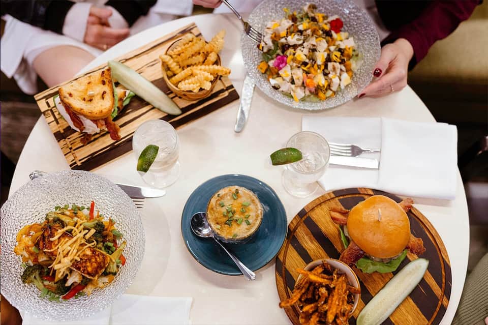 Overhead view of restaurant table with gourmet dishes, sandwich, salad, soup, and beverages served on white tablecloth