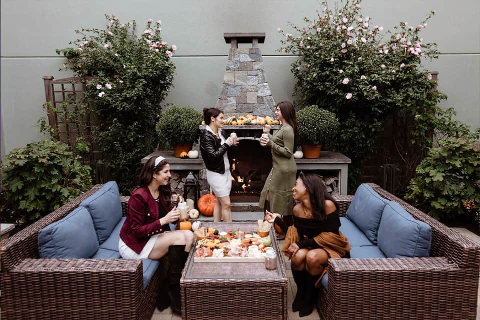 Outdoor patio with fireplace, guests socializing, fall decor, and climbing flowers on walls