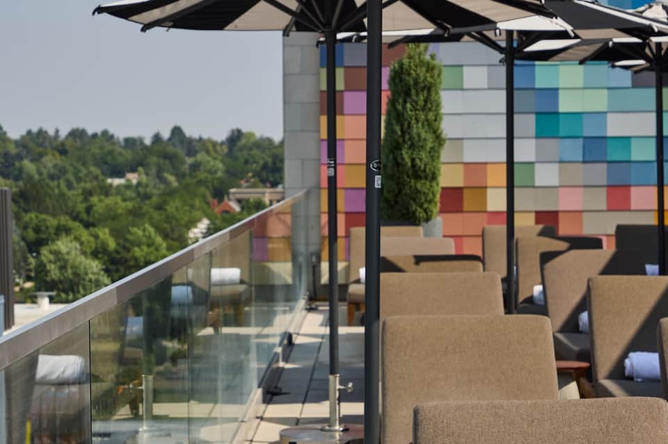 Modern rooftop terrace with colorful grid wall art, black umbrellas, lounge chairs, and forest views