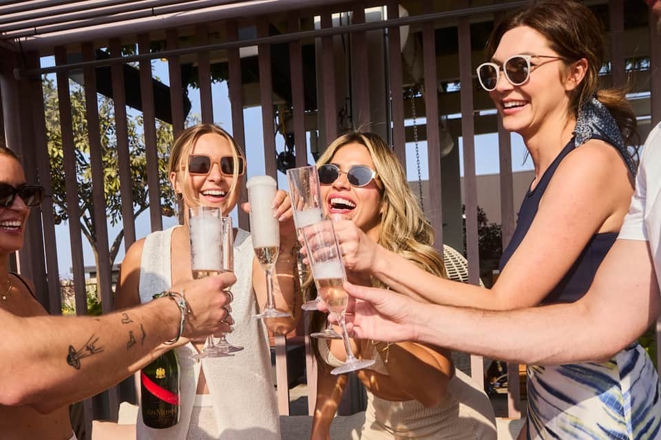 Group of women toasting with champagne glasses on resort balcony with ocean backdrop