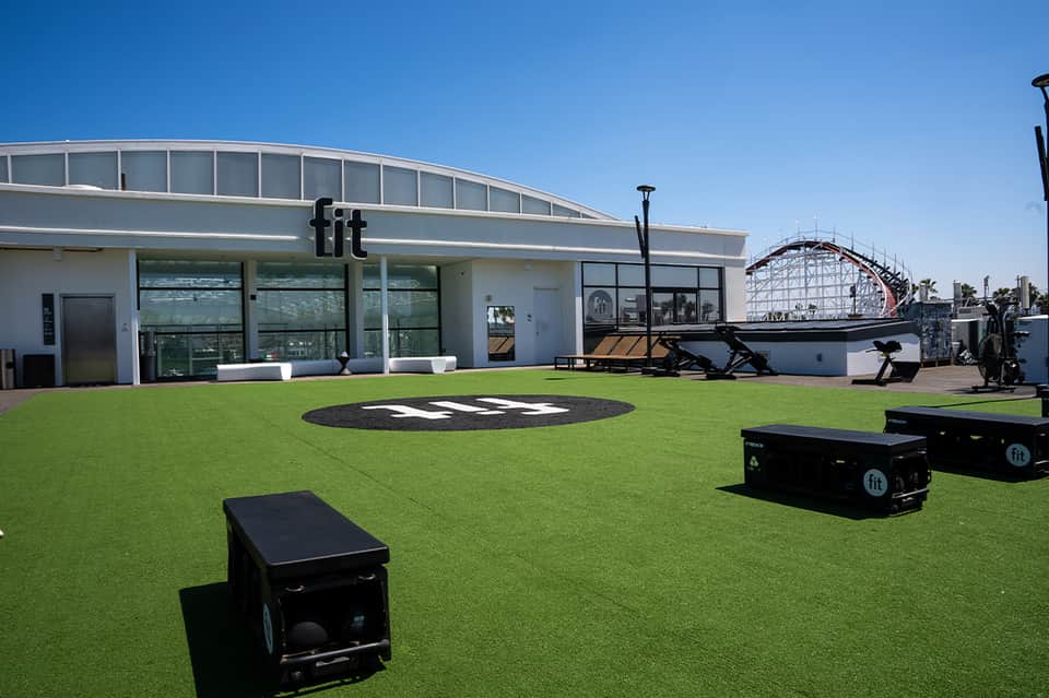 Fit gym facility with artificial turf, outdoor fitness equipment, and roller coaster in background