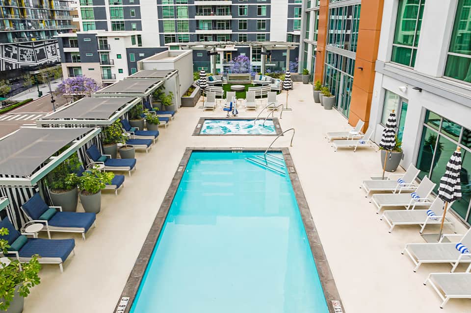 Urban rooftop pool deck with lap pools, blue lounge chairs, and surrounding apartment buildings