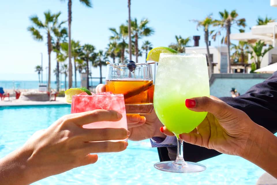 Three colorful cocktails by poolside with palm trees and ocean view in background