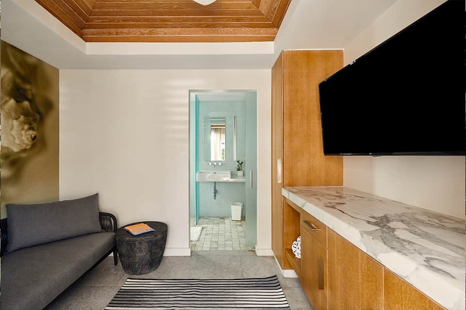 Modern hotel room with gray sofa, wooden ceiling details, marble countertop, and flat-screen TV