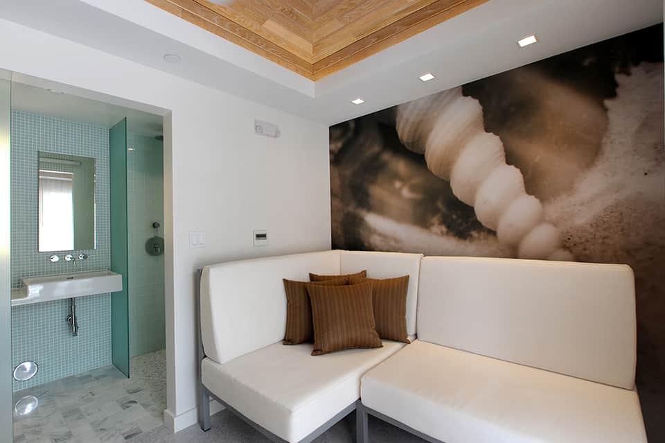 Spa bathroom with turquoise tile shower, white seating area, wooden ceiling, and nature wall art