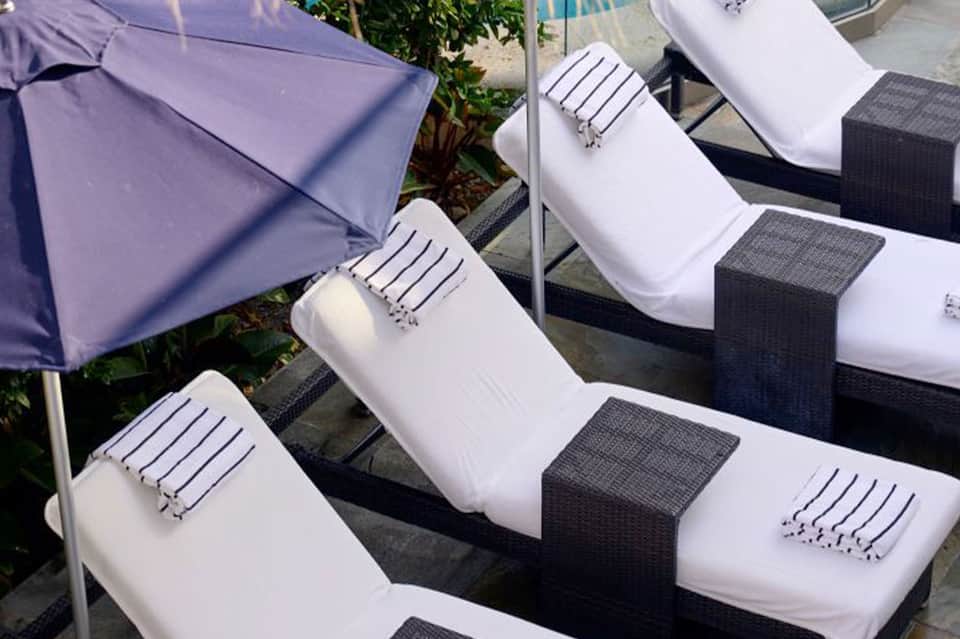 Close-up of lounge chair cushions with white and dark accents beside a purple umbrella by the pool
