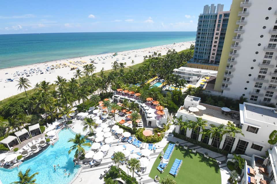 Beachfront resort with ocean view, pool area, palm trees, lounge chairs, and sandy beach