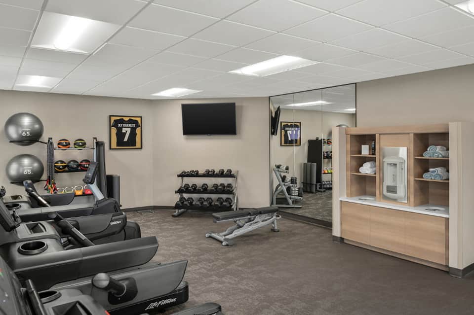 Fitness center with cardio equipment, dumbbells, mirrors, and framed sports memorabilia