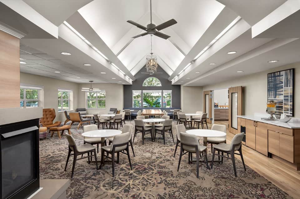 Modern lounge with vaulted ceiling, fireplace, round tables, and floor-to-ceiling windows